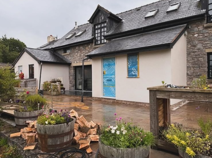 Cream rendered house extension with stone walls, slate roof and patio